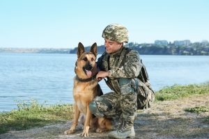 Man in military uniform with German shepherd dog near river